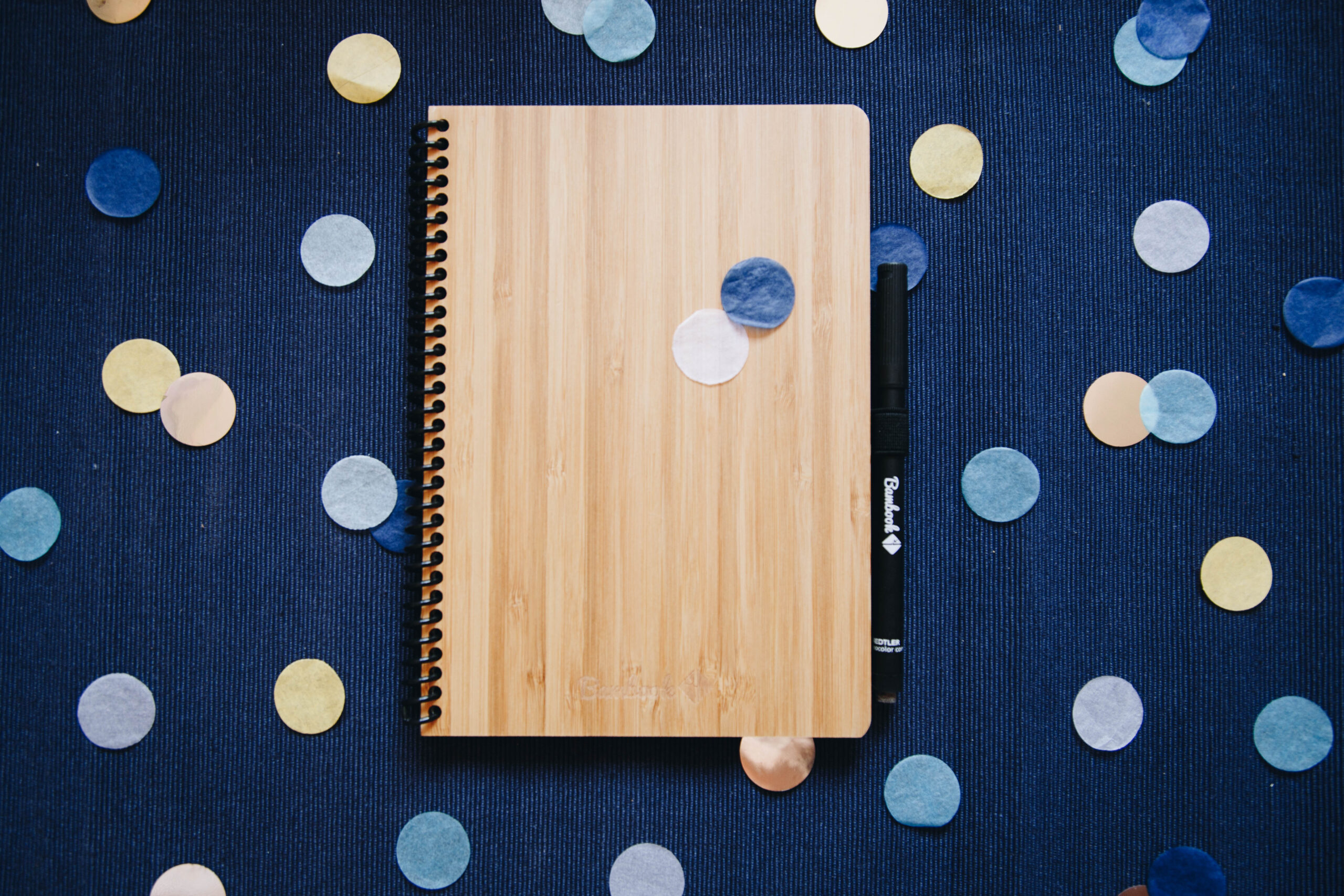 Flatlay foto van een houten notitieboek met geel/blauwe confetti