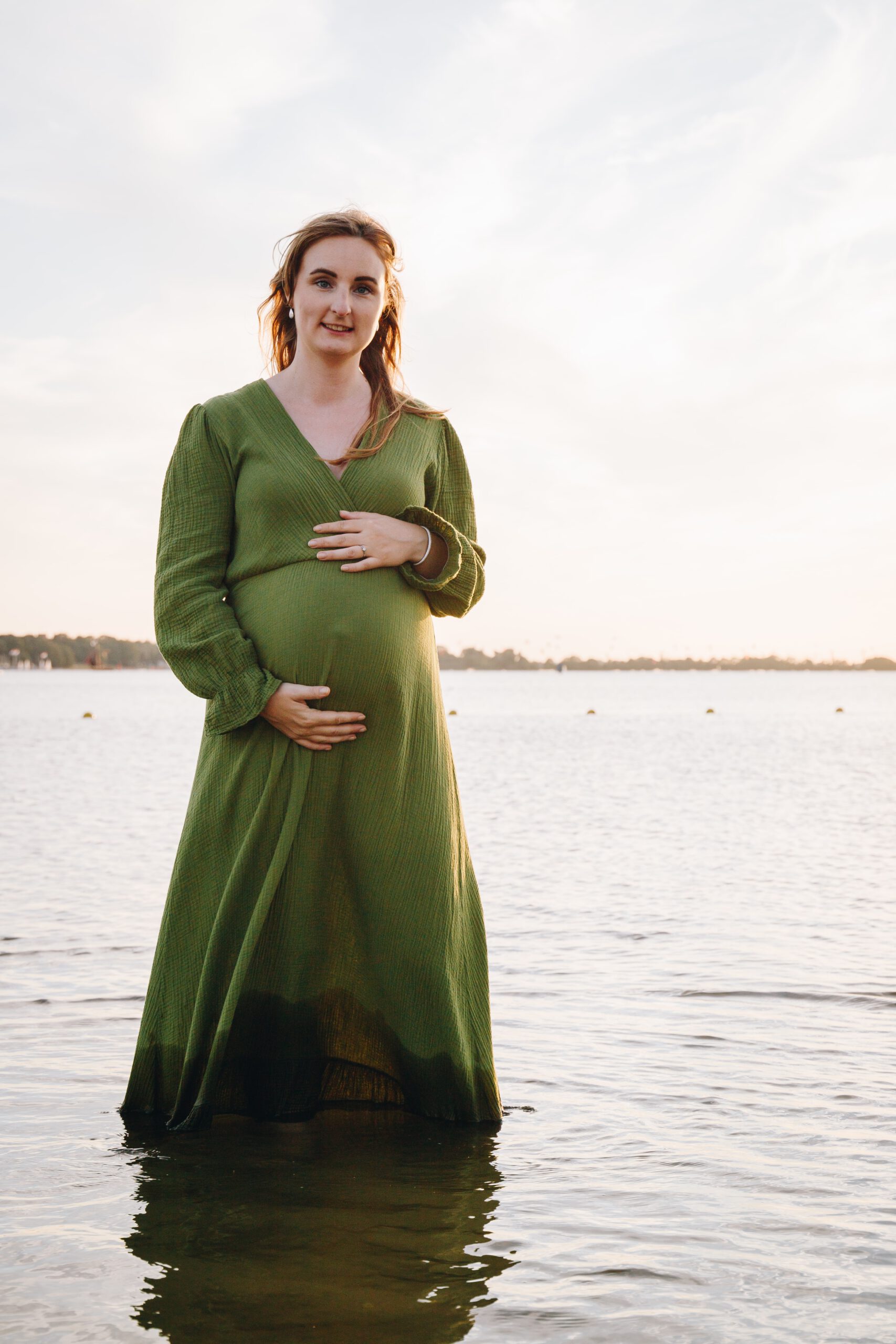 Aanstaande moeder in de zee met zwangere buik en groene jurk