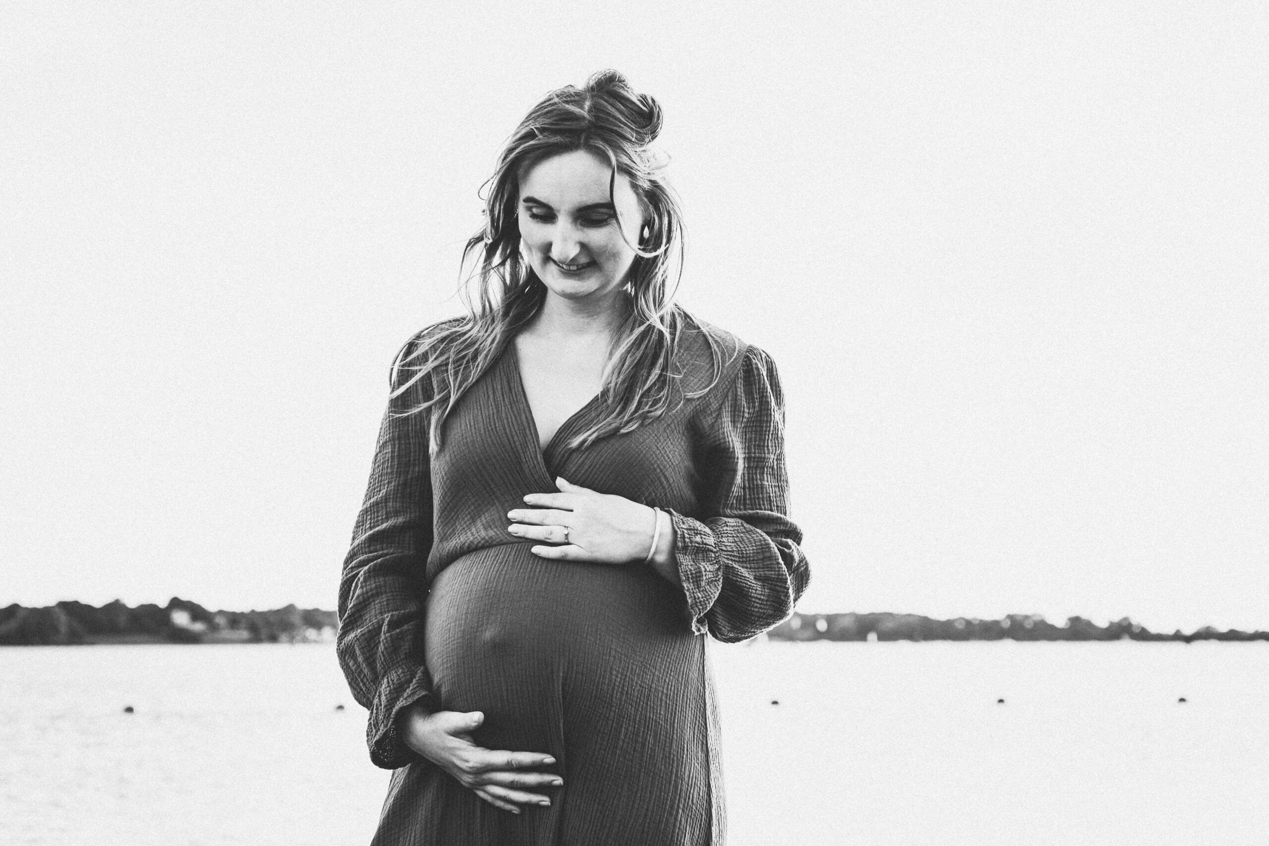 Zwart wit foto van aanstaande moeder vol trost in de zee met haar handen liefkozend om haar zwangere buik 