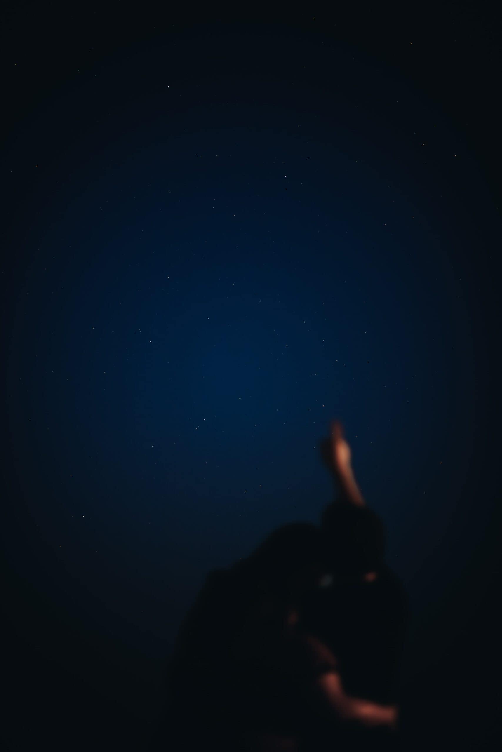 Nachtfotografie gecombineerd met portretfotografie waarin we twee mensen zien waarvan de man naar de sterren wijst terwijl ze elkaar omarmen