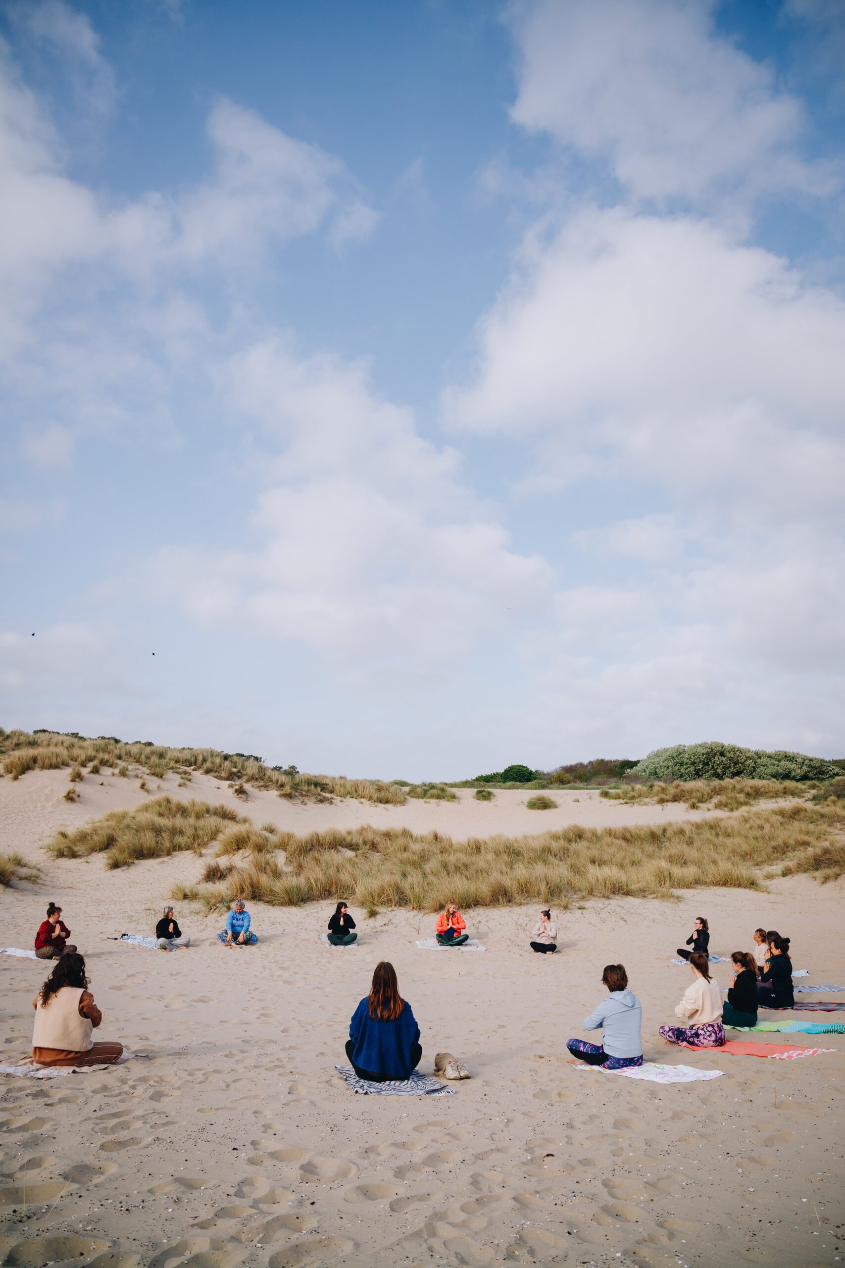 Rechtopstaande foto van een cirkel dames op yoga maten in de zonnige duinen bij Scheveningen
