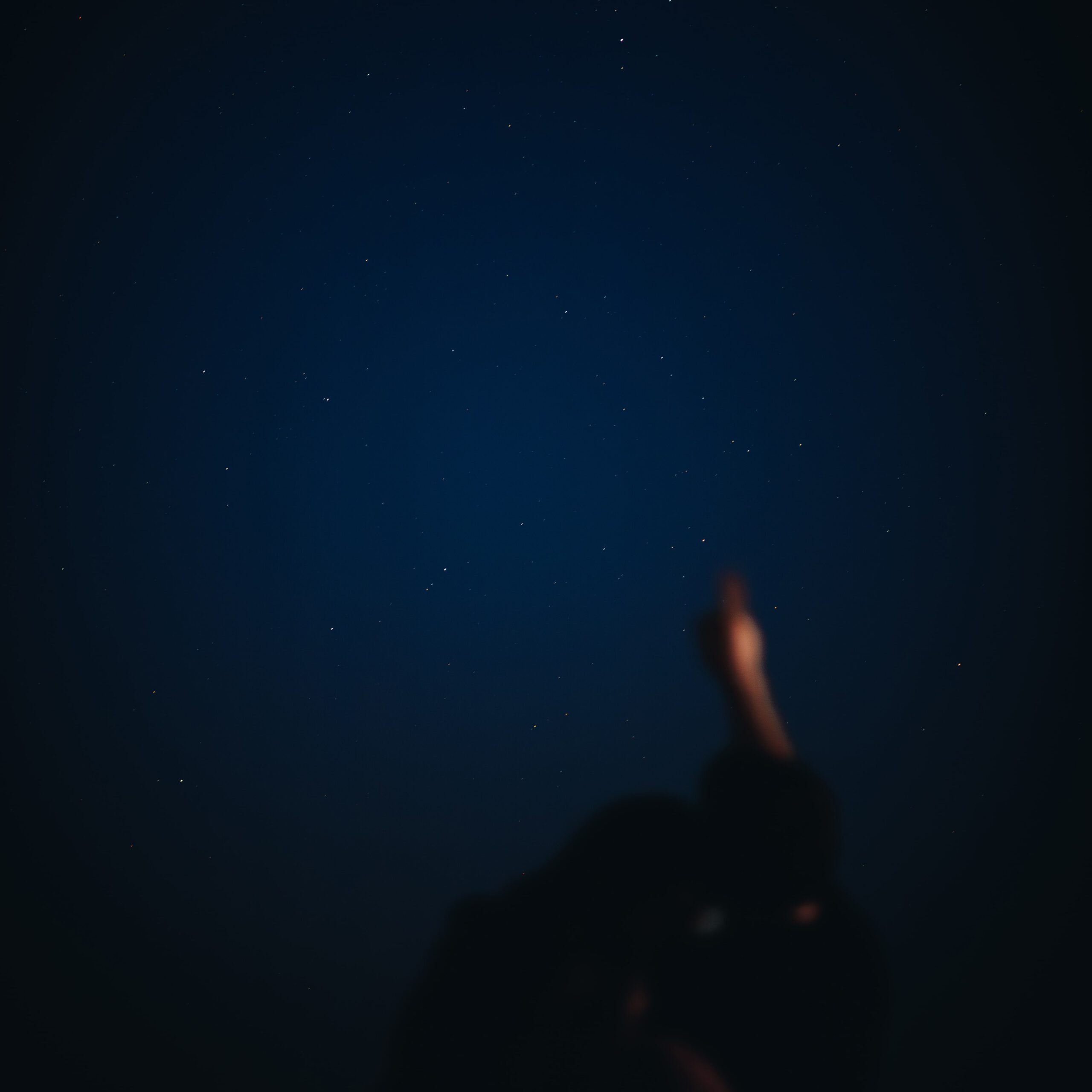 Foto van een wijzend stel onder een heldere sterrenhemel, de sterren zijn scherp en het stel beetje blurry op de voorgrond