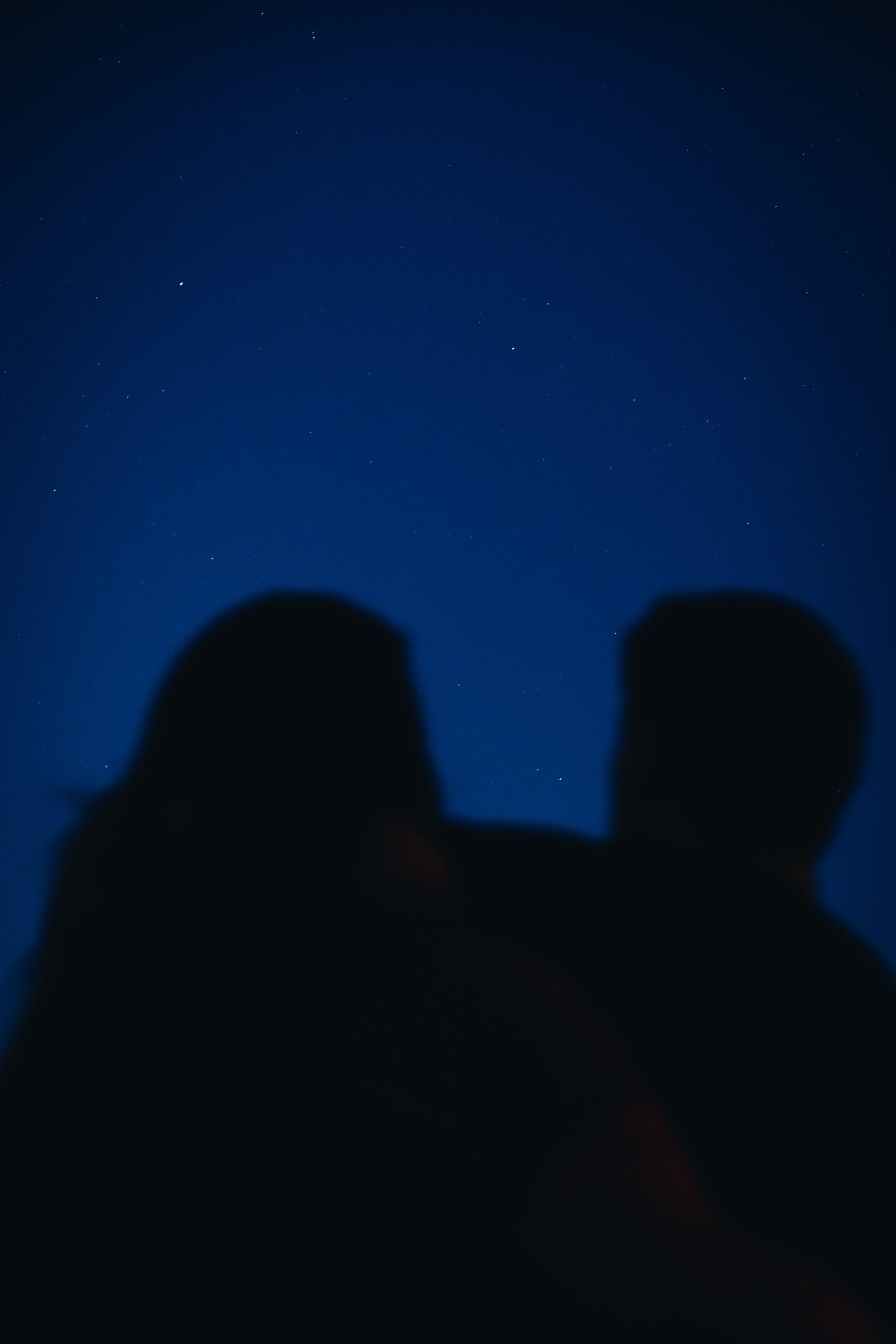 Foto van een stel onscherp op de voorgrond tegen de heldere sterrenhemel op de achtergrond